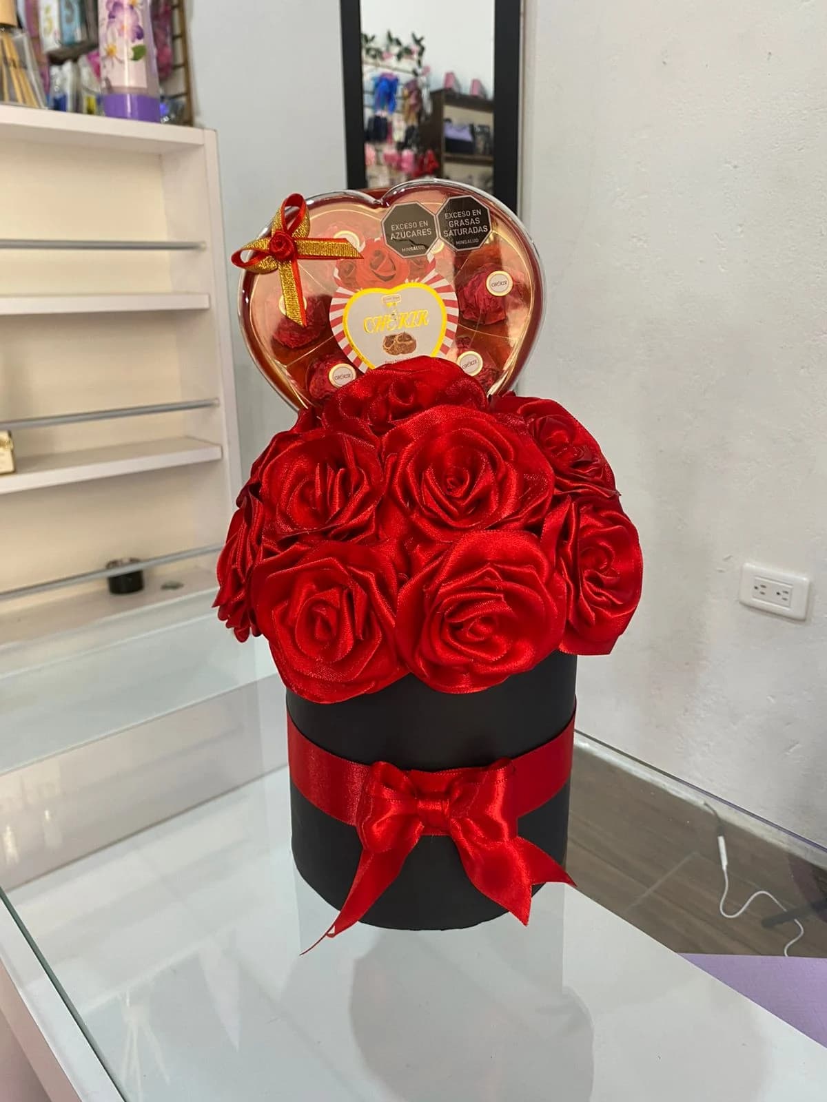 Ramo de rosas rojas en caja negra con lazo, acompañado de una caja de chocolates en forma de corazón